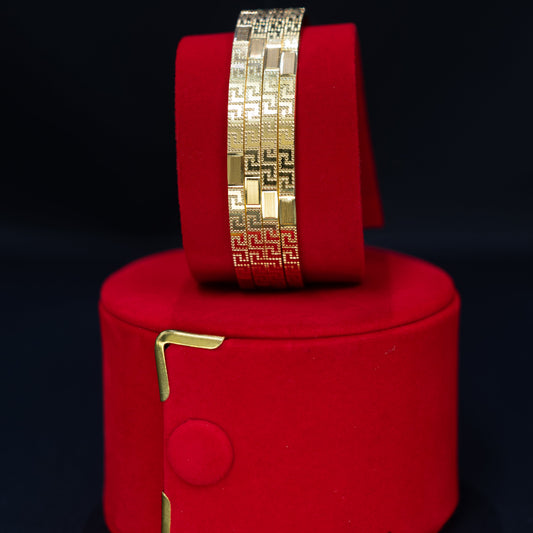 A gold geometric link bracelet displayed on a red cylindrical velvet stand against a black background.