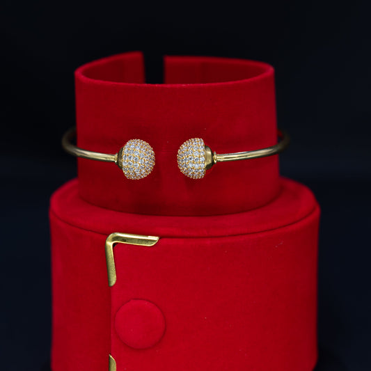 A pair of gold bangle bracelets with round pavé-set crystal clusters, displayed on a red velvet jewelry stand against a black background.