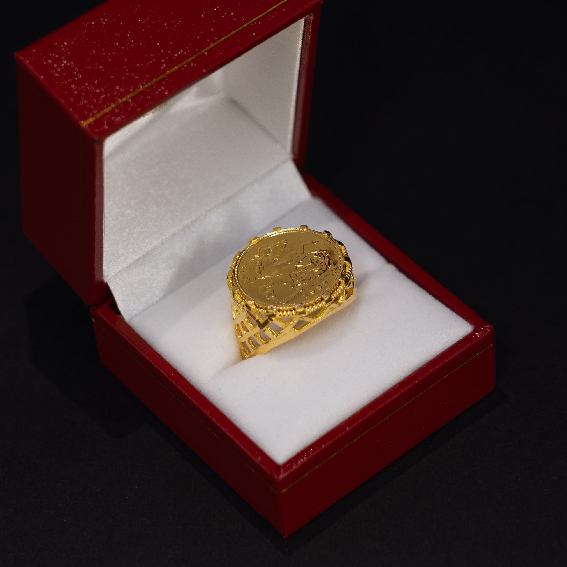 A textured yellow gold signet ring displayed inside an open red velvet jewelry box with a white interior, set against a solid black background.
