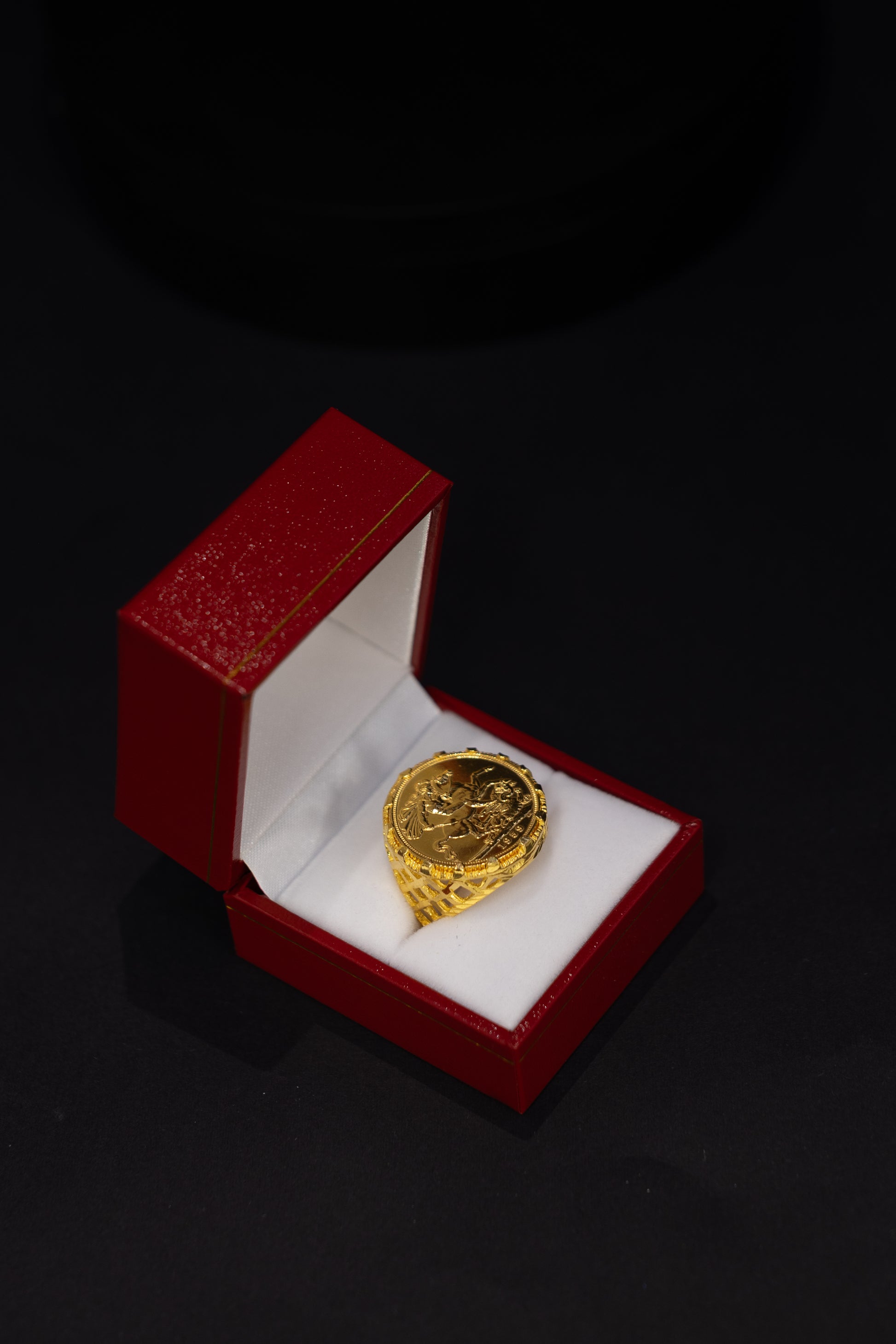 A gold ring displayed inside an open red jewelry box with a white insert, set against a dark black background.