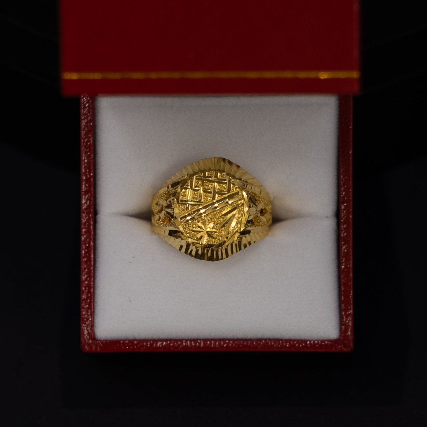 A gold signet ring with an embossed crest, presented inside an open red jewelry box with a white velvet cushion against a black background.