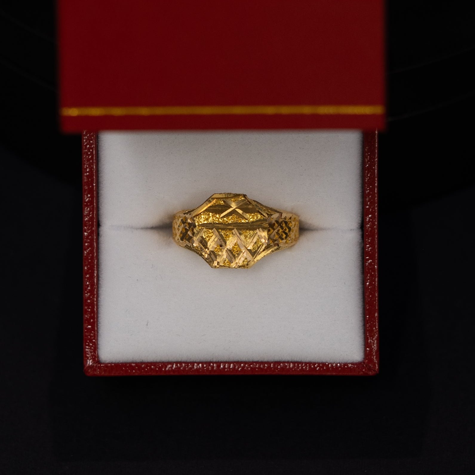 A small gold ring displayed inside an open red jewelry box with a white interior, set against a dark black background.