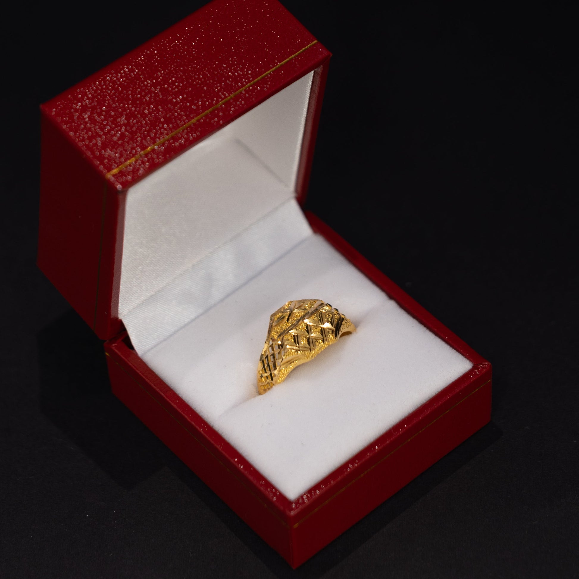 A textured yellow gold ring displayed inside an open red jewelry box with a white velvet lining, set against a solid black background.