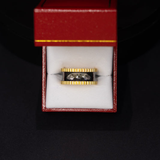 A gold and black ring displayed inside an open red jewelry box with a white interior, set against a dark black background.