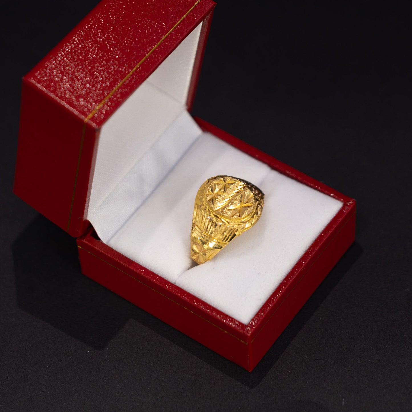 A textured yellow gold ring displayed inside an open red jewelry box with a white insert, set against a dark black background.
