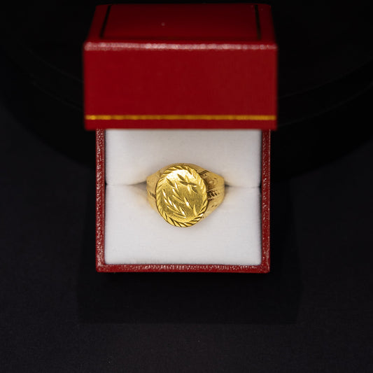 A gold ring with an oval face, displayed inside an open red jewelry box with a white interior, set against a dark black background.