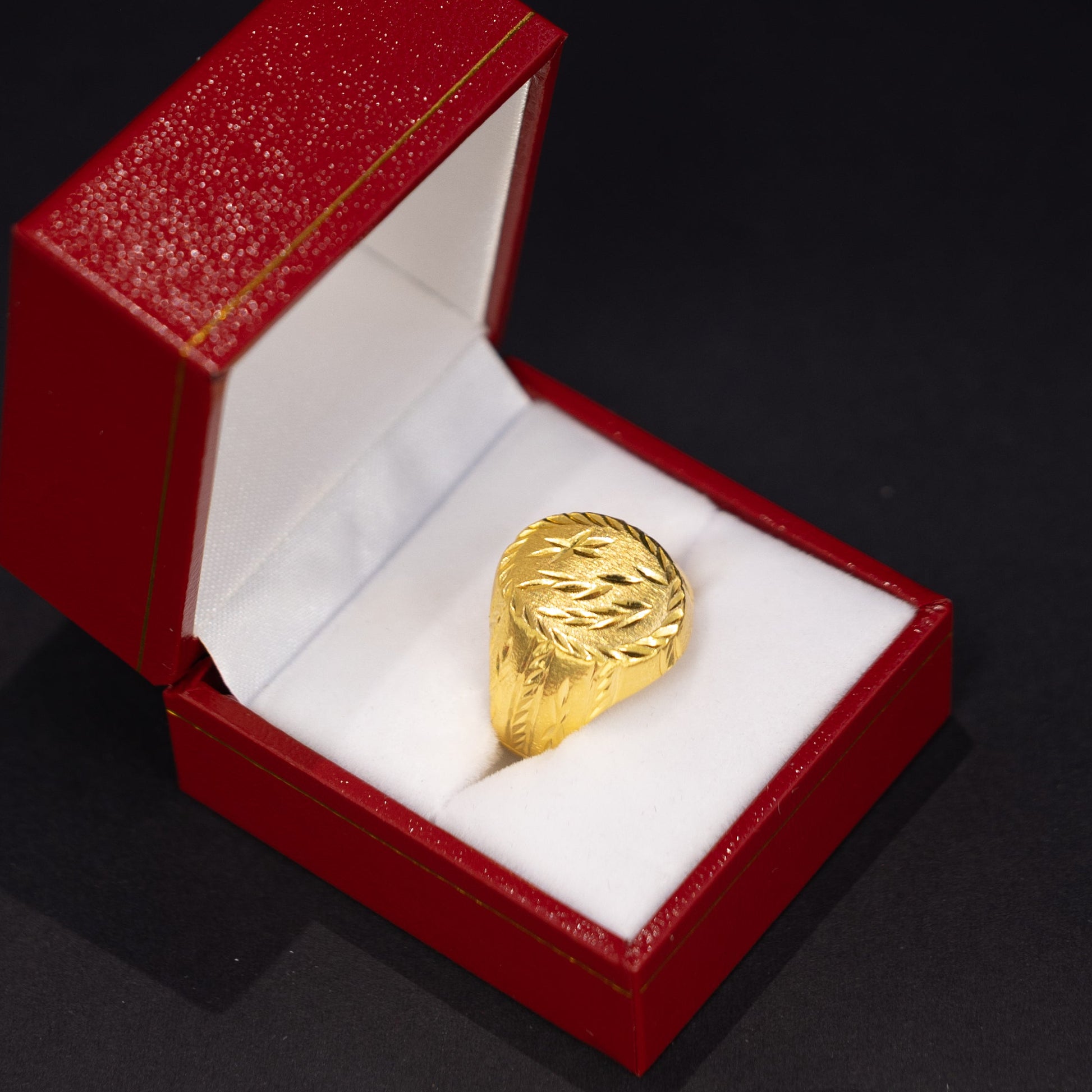 A textured gold ring displayed inside an open red jewelry box with a white lining, set against a dark black background.