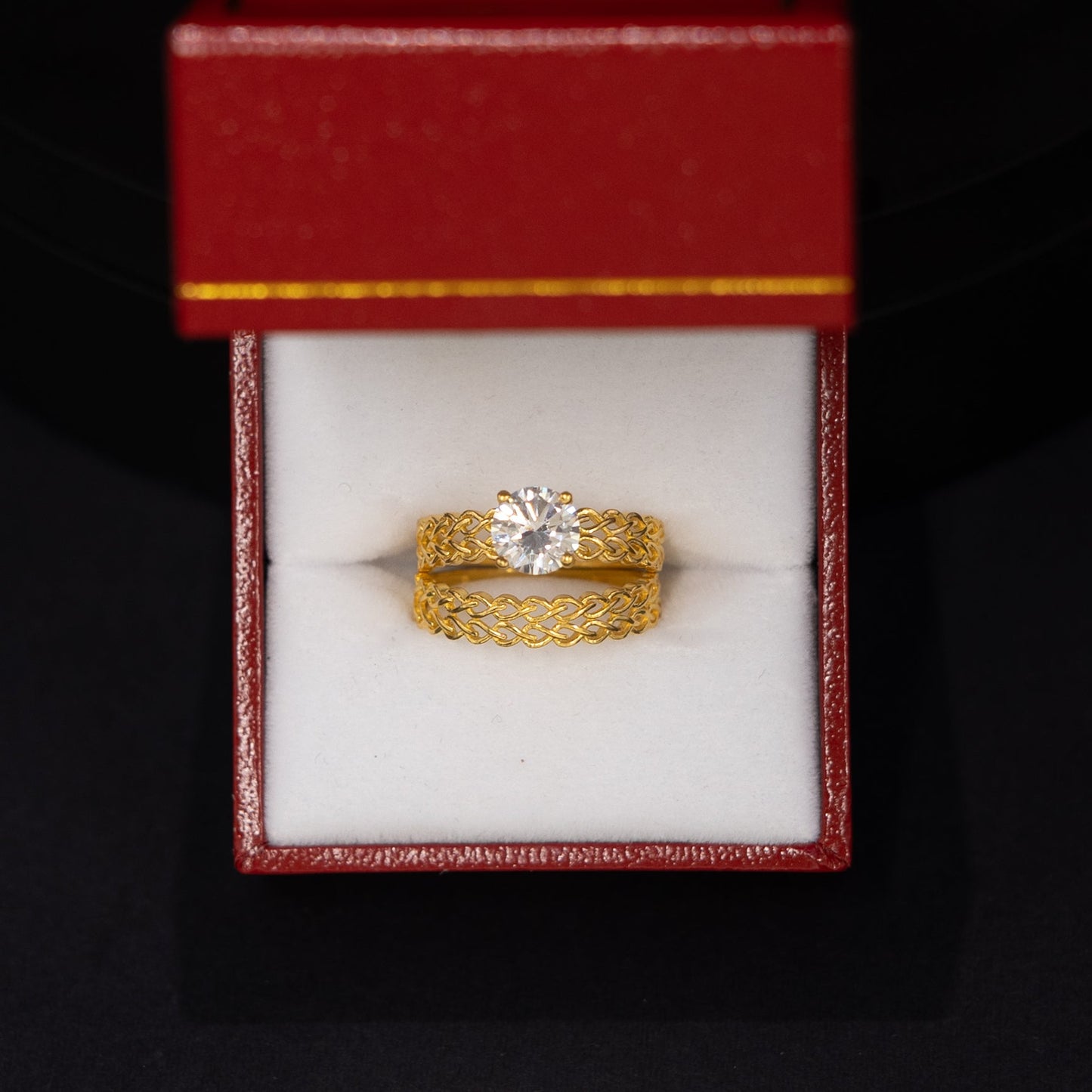 A yellow gold ring with a clear center stone displayed inside an open red jewelry box on a black background.