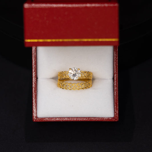 A yellow gold ring with a clear center stone displayed inside an open red jewelry box on a black background.