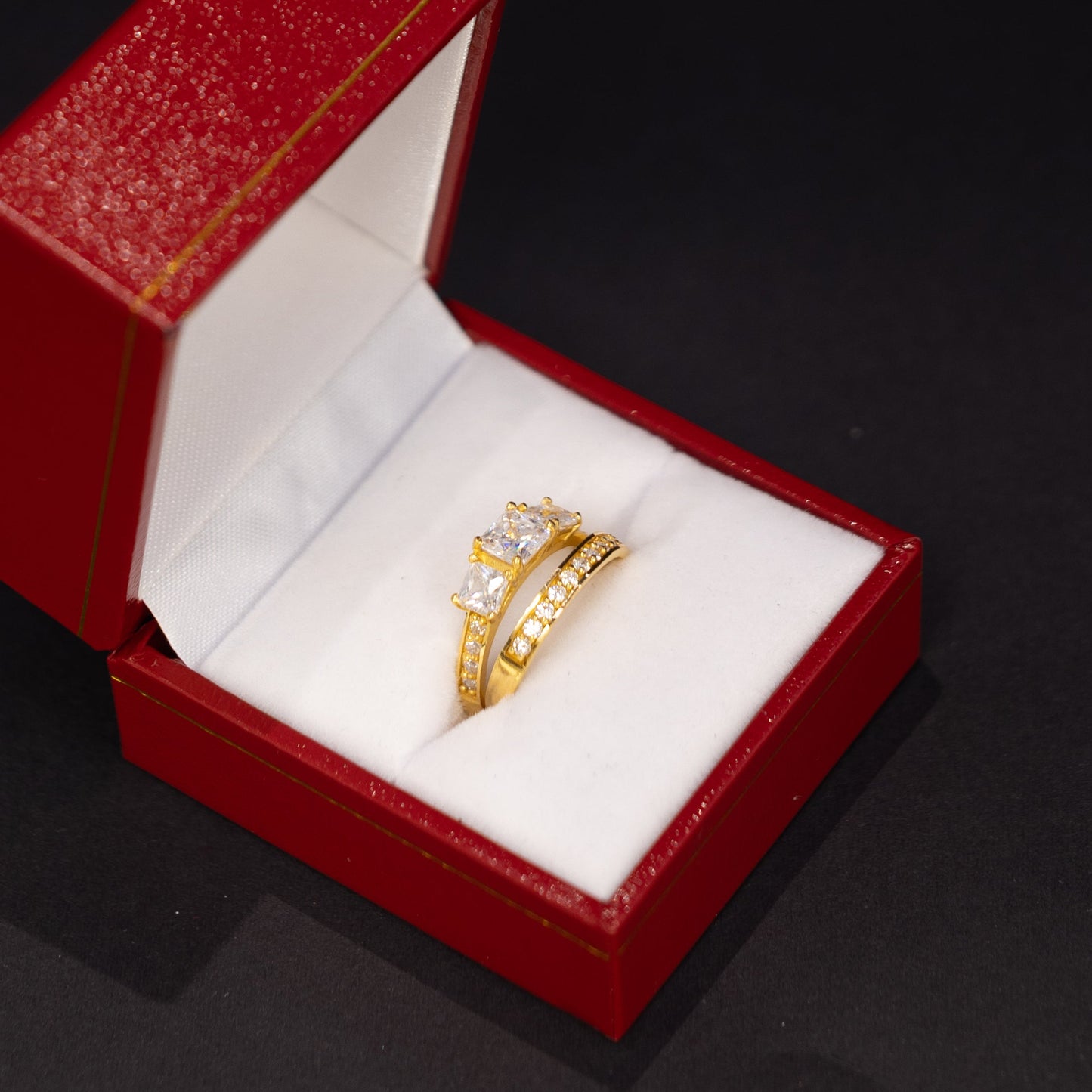 A gold ring with clear gemstones displayed inside an open red jewelry box on a dark background.