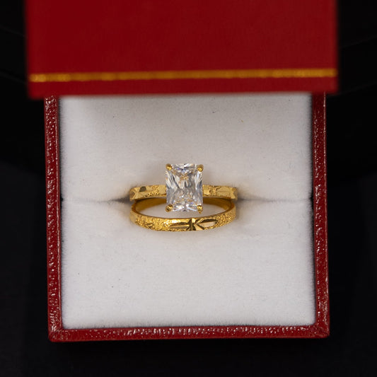 A yellow gold ring with a central clear gemstone displayed inside an open red jewelry box with a white interior, set against a dark black background.
