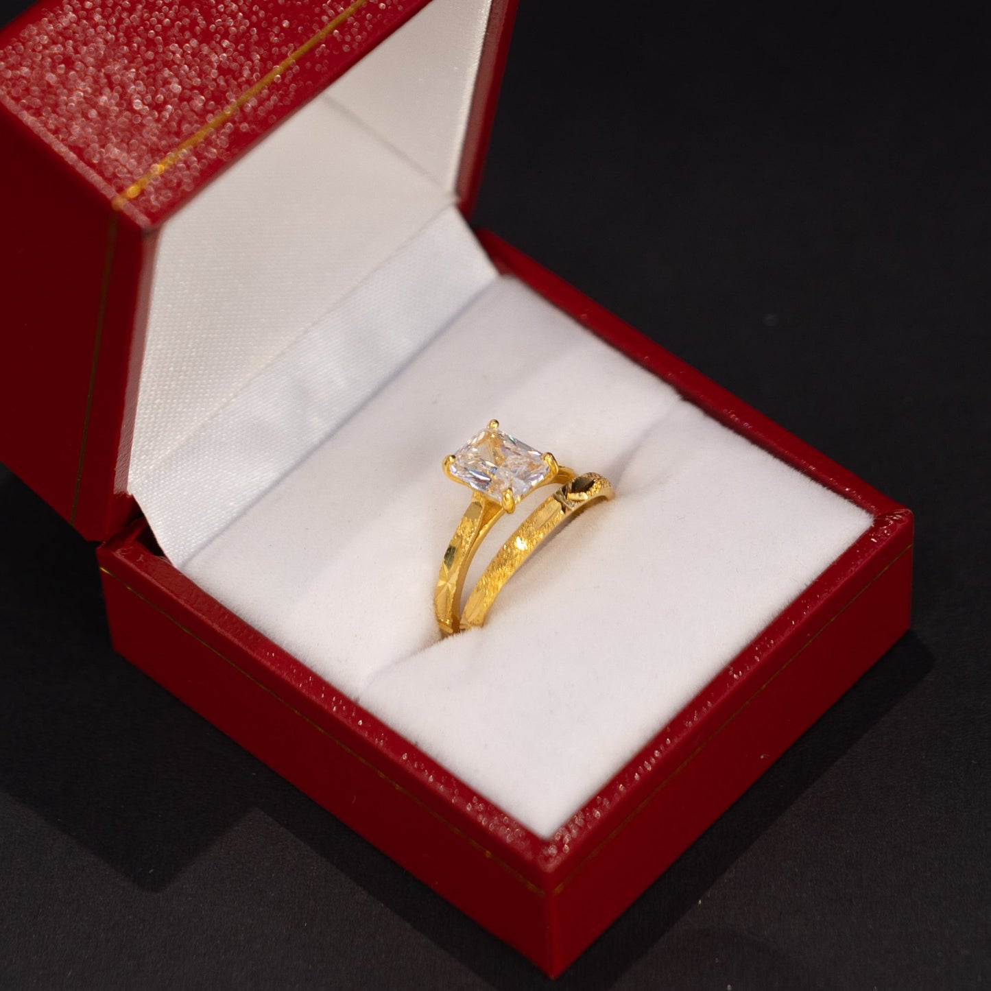 A gold ring with a clear central gemstone displayed inside an open red jewelry box with a white cushion, set against a dark background.