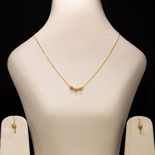 Gold necklace and matching drop earrings displayed on a white jewelry bust against a black background.