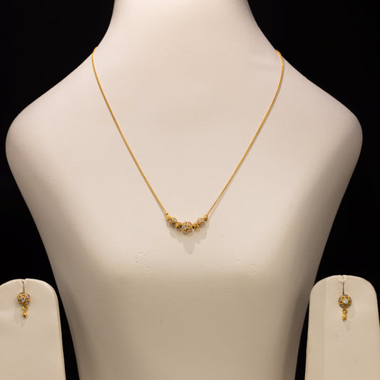 Gold necklace and matching earrings displayed on a white jewelry bust against a black background.
