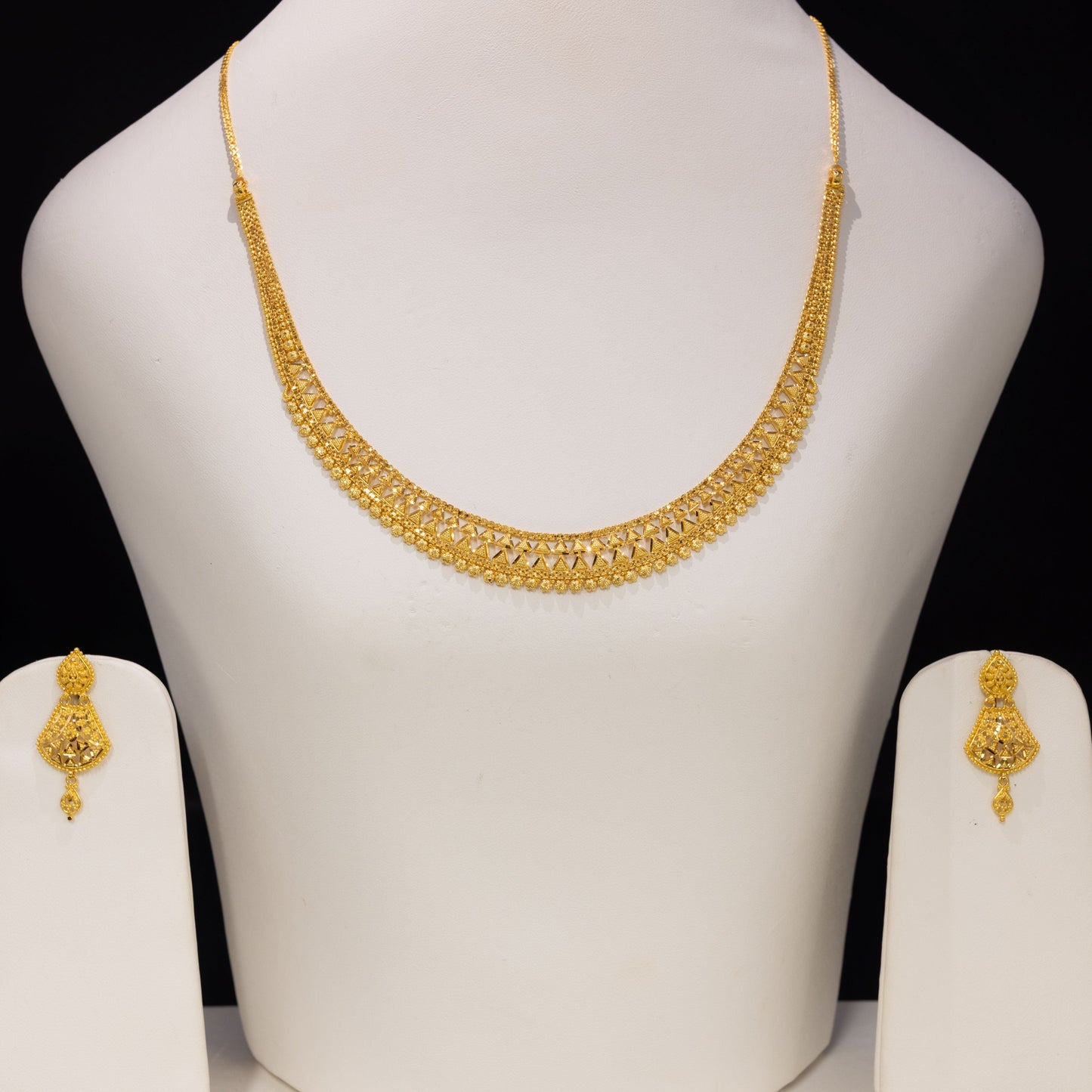 Gold necklace and matching earrings displayed on a white jewelry bust against a black background.