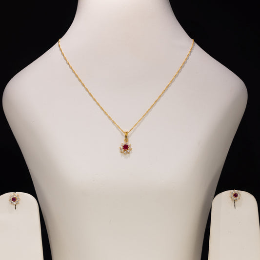 Gold necklace with a red and white floral pendant displayed on a white jewelry bust, with matching stud earrings on side stands against a black background.