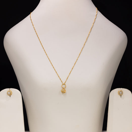 A gold necklace with a small pendant displayed on a white jewelry bust, with matching stud earrings shown on side stands against a black background.