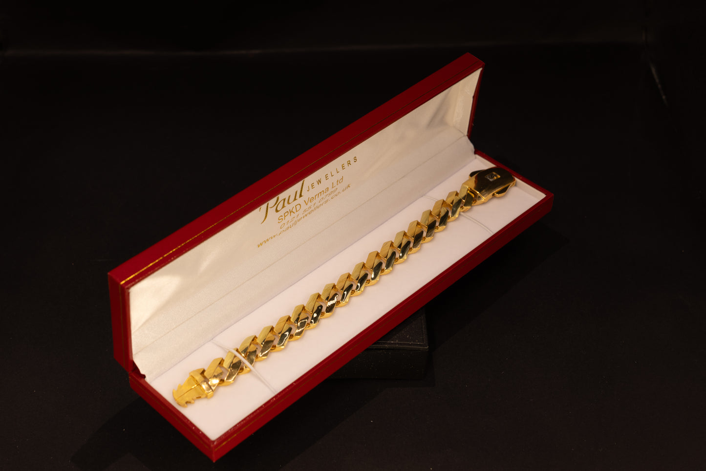 A gold-toned Cuban link bracelet displayed inside an open red presentation box with a white interior. 