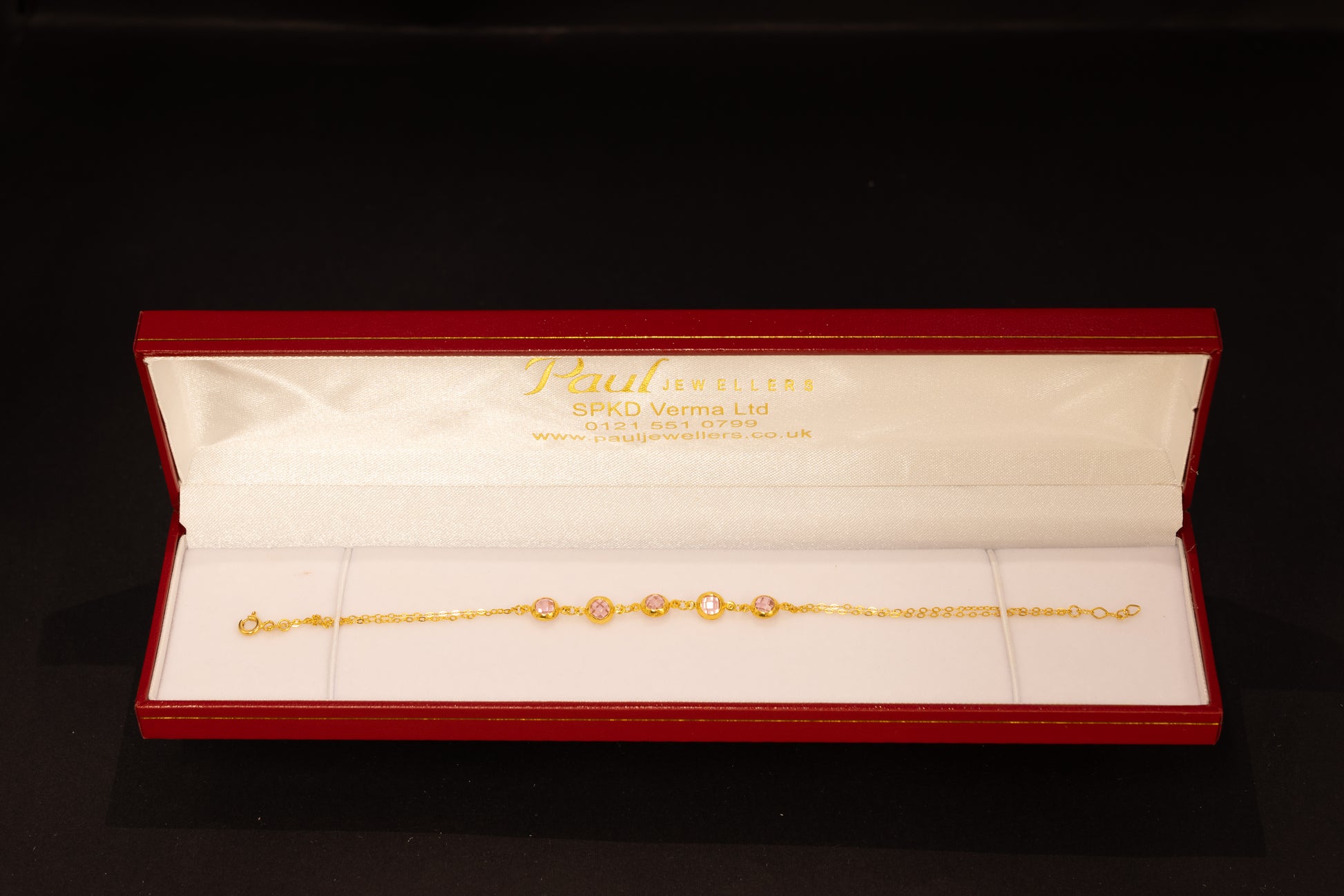 A delicate gold chain bracelet with oval-cut clear stones, presented in an open red Jewellery gift box on a black background.
