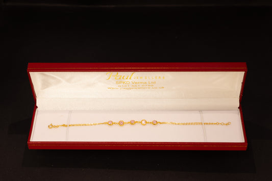 A delicate gold chain bracelet with oval-cut clear stones, presented in an open red Jewellery gift box on a black background.
