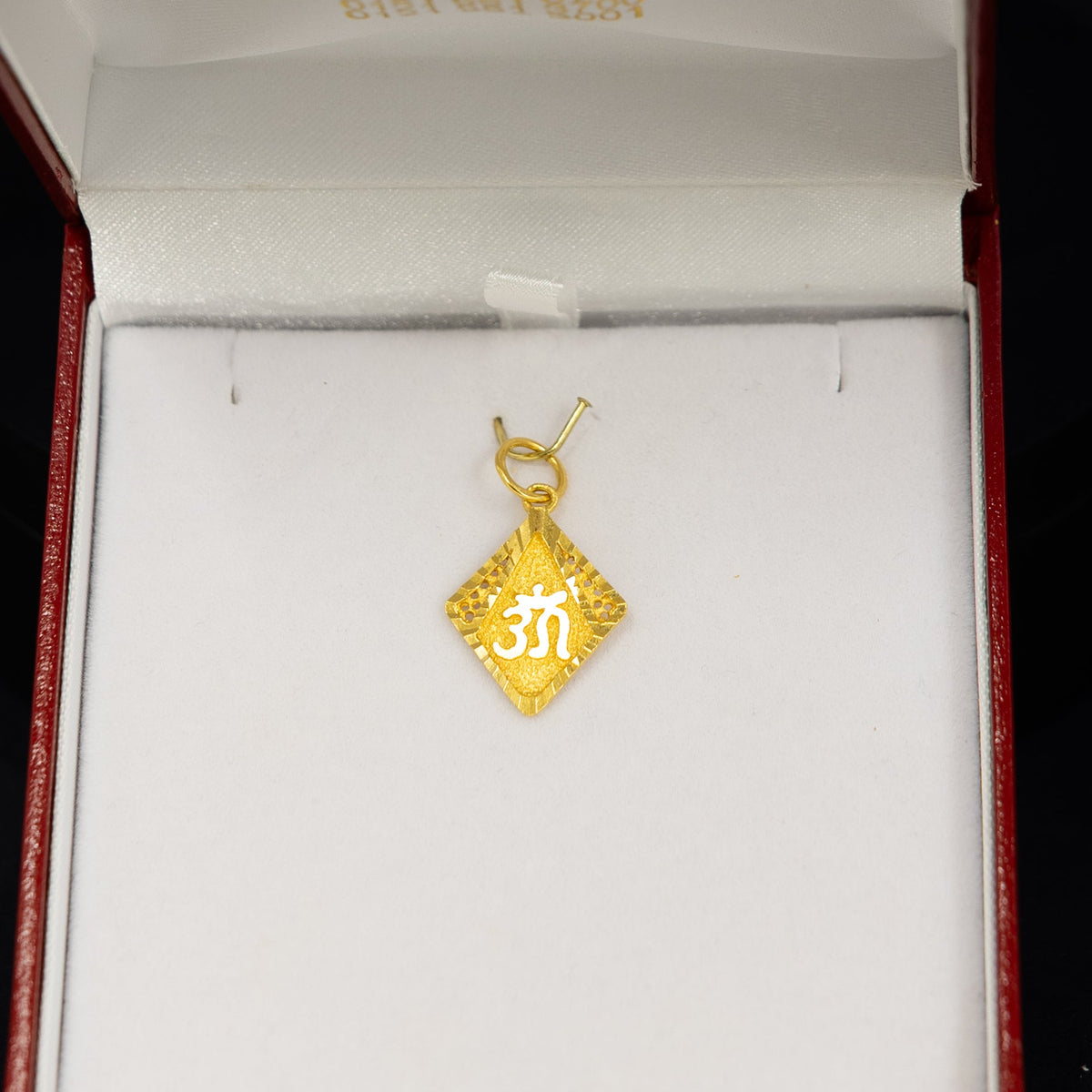 A small gold pendant with a diamond-shaped cutout and the number '39' in the center, displayed inside an open red jewelry box with a white insert against a black background.